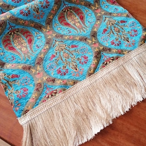 May include: A blue and gold table runner with a paisley pattern and fringe trim.