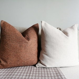 May include: Two decorative throw pillows on a couch. One pillow is brown with a textured fabric and the other is white with a textured fabric.
