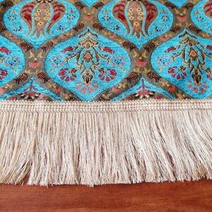 May include: A blue and brown patterned table runner with a white fringe. The runner has a traditional design with floral motifs.