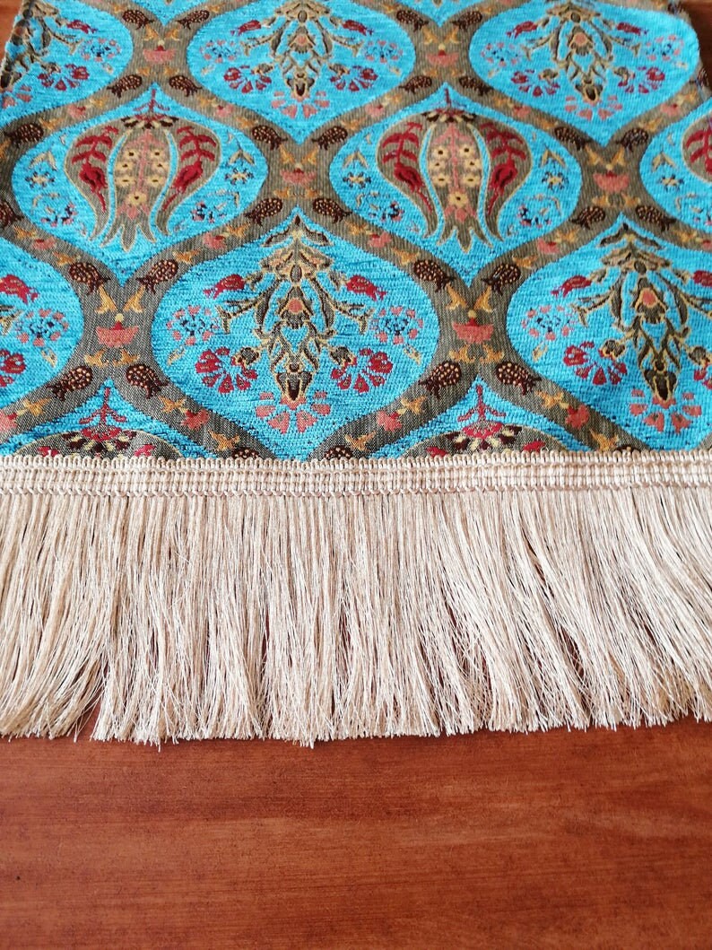 May include: A blue and brown patterned table runner with a white fringe. The runner has a traditional design with floral motifs.