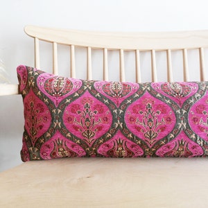 May include: A long, pink and green patterned lumbar pillow with a floral design. The pillow is on a light wood chair.