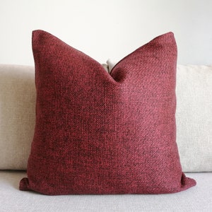 May include: A burgundy throw pillow with a textured fabric. The pillow is on a light beige couch.