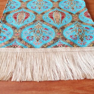 May include: A blue and gold table runner with a floral pattern and a fringe border. The runner is made of a woven fabric and has a traditional design.