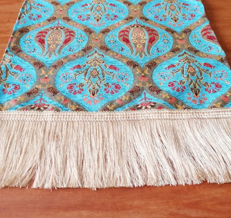 May include: A blue and gold table runner with a floral pattern and a fringe border. The runner is made of a woven fabric and has a traditional design.