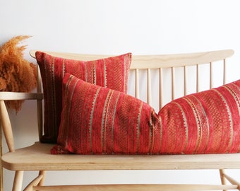 May include: Two red and gold striped throw pillows on a light wood bench. The pillows have a woven texture and a geometric pattern.