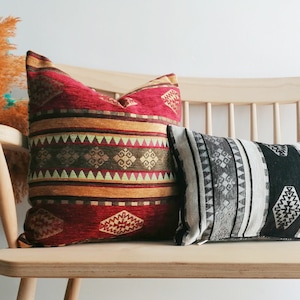 May include: Two decorative throw pillows with geometric patterns. The pillow on the left is red, gold, and green with a striped pattern. The pillow on the right is black, white, and gray with a striped pattern.