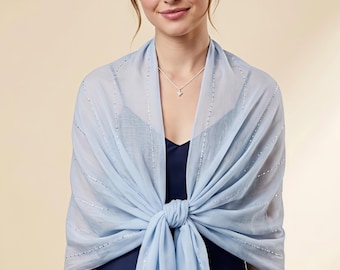 May include: A light blue sheer shawl featuring vertical rows of delicate silver sequins. The lightweight fabric is draped over the shoulders and tied in a knot at the front, showcasing a subtle shimmer across the translucent material.