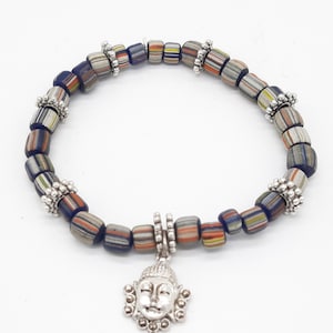 Könnte beinhalten: Ein blaues und orangefarbenes Perlenarmband mit einem silbernen Buddha-Anhänger. Die Perlen sind mehrfarbig und haben ein gestreiftes Muster.