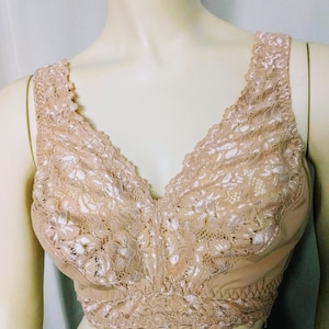 May include: A beige bralette with a V-neck design. The bralette features a delicate floral lace overlay on the cups and straps, with a scalloped edge. The fabric appears soft and comfortable, suitable for everyday wear.