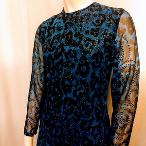 May include: A teal and black patterned dress with long sleeves. The dress features a high neckline and is adorned with sequins. The sleeves are sheer, and the pattern resembles a leopard print. The dress is displayed on a mannequin.