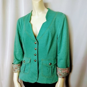 May include: A teal blazer with three-quarter sleeves, gold buttons, and two front pockets. The cuffs are turned up, revealing a floral patterned lining. The blazer is displayed on a mannequin.