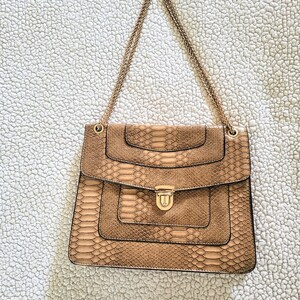 May include: A tan faux snakeskin handbag with a gold chain strap. The rectangular bag has a flap closure with a gold-tone clasp. The bag's design features layered panels and a textured pattern.