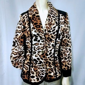May include: A leopard print blazer with black trim and three brown buttons. The jacket features a classic collar and is displayed on a mannequin. The pattern includes shades of brown, tan, and cream.