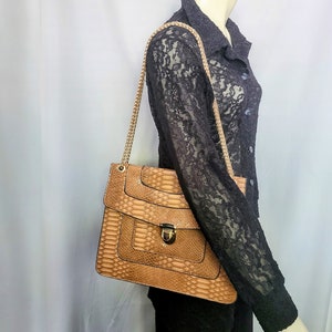 May include: A tan handbag with a snakeskin pattern and a gold chain strap. The bag has a rectangular shape with a flap closure and a gold-colored clasp. The bag is carried over the shoulder.