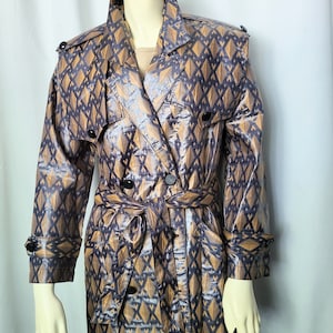 May include: A patterned trench coat in shades of brown and navy blue. The coat features a geometric diamond design, a belted waist, and black buttons. The coat is displayed on a mannequin.