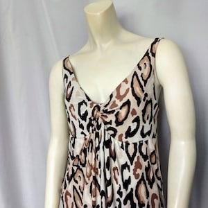May include: A sleeveless dress with a V-neckline and a gathered waist. The dress features a leopard print pattern in shades of brown, black, and cream. The dress is displayed on a mannequin.