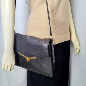 May include: A dark gray leather handbag with a gold-colored clasp and shoulder strap. The bag has a rectangular shape with a flap closure. The strap is thin and black.