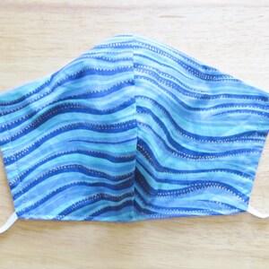 May include: A blue and turquoise face mask with a wavy pattern and gold glitter accents.
