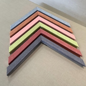 May include: A selection of colourful wooden picture frame corners arranged in a chevron pattern. The frames display a variety of colours, including blue, brown, pink, green, and red. The wood grain texture is visible on each frame.