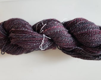 May include: A skein of dark purple yarn with flecks of grey and white. The yarn is soft and fluffy, and it would be perfect for knitting or crocheting a cozy scarf or sweater.