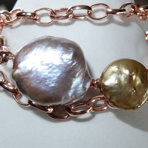 May include: Rose gold chain bracelet featuring two large, irregularly shaped pearls. One pearl is a silvery-gray color, and the other is a golden hue. The bracelet has a double-strand design with a textured chain.