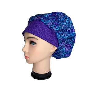 Puede incluir: Un gorro de exfoliación abullonado con estampado azul y morado. El gorro presenta una banda morada oscura con un diseño arremolinado y una corona de patrones florales azules y morados. El gorro se muestra en una cabeza de maniquí.