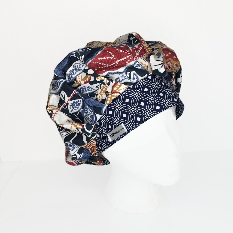 Puede incluir: Un gorro de exfoliaci&oacute;n abullonado estampado con interior blanco. El gorro presenta una mezcla de estampados florales y geom&eacute;tricos en azul marino, rojo y dorado. Una peque&ntilde;a etiqueta con texto es visible en la parte delantera. El gorro se muestra en una cabeza de maniqu&iacute; blanca.