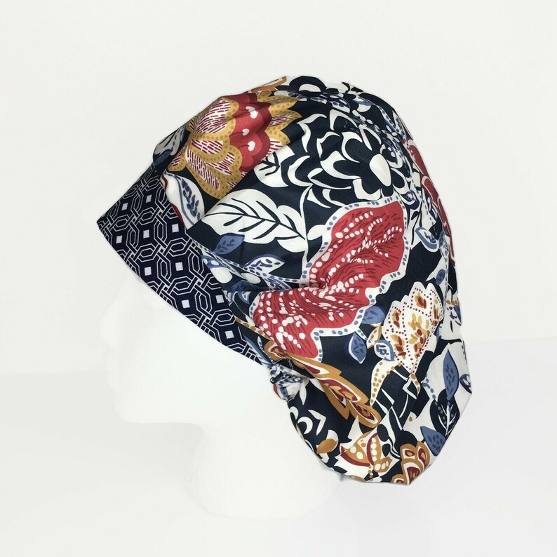 Puede incluir: Un gorro quir&uacute;rgico con estampado floral con fondo azul marino y dise&ntilde;os florales rojos, blancos y dorados. El borde tiene un dise&ntilde;o geom&eacute;trico en azul marino y blanco. El gorro es de tela.