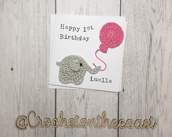 May include: A handmade crochet card with a gray elephant holding a pink balloon. The card says "Happy 1st Birthday Luella" and is signed "@CrochetonTheCoast".