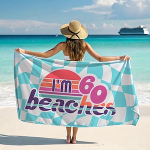 May include: A beach towel with a checkered pattern in white and turquoise, featuring the text "I'm 60 beaches" in purple and pink. The towel has a retro sunset design in the center.