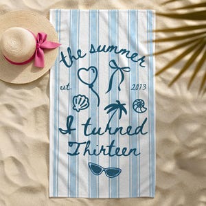 May include: A white and light blue striped beach towel featuring dark blue text that reads the summer est. 2013 I turned Thirteen, accompanied by illustrations of a heart balloon, a bow, a seashell, a palm tree, a spiral shell, and sunglasses.