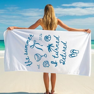 Pu&ograve; includere: Un telo mare bianco con testo blu scuro che recita "the summer est. 2026 I turned Retired" insieme a illustrazioni grafiche di un nastro, un calice da vino, una conchiglia, una palma, un nautilus e un paio di infradito.