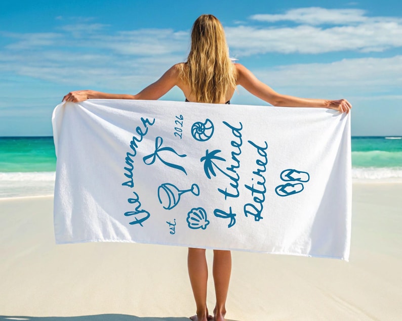 Pu&ograve; includere: Un telo mare bianco con testo blu scuro che recita "the summer est. 2026 I turned Retired" insieme a illustrazioni grafiche di un nastro, un calice da vino, una conchiglia, una palma, un nautilus e un paio di infradito.