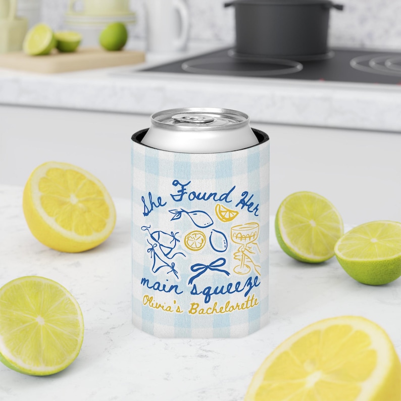 May include: A blue and white checkered can cooler with the text "She Found Her Main Squeeze Olivia's Bachelorette" in blue and gold. The cooler is surrounded by lemon and lime halves.