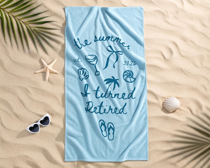 Pu&ograve; includere: Un telo mare rettangolare azzurro con testo blu scuro che recita the summer est. 2026 I turned Retired, accompagnato da illustrazioni grafiche di un calice da vino, un fiocco, una palma, conchiglie e un paio di infradito.