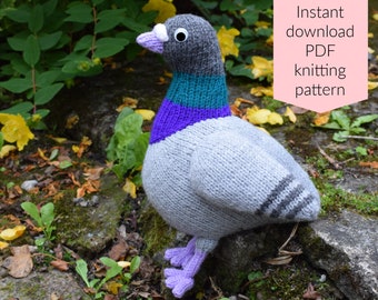 May include: Knitted gray pigeon with purple, teal, and white accents. The pigeon is sitting on a rock with green moss and brown leaves. Instant download PDF knitting pattern.