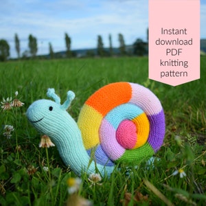 May include: A colorful knitted snail toy with a rainbow shell. The snail is sitting in a grassy field. Instant download PDF knitting pattern.