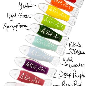 May include: A set of ten glass wish fish ornaments in various colors, including red, orange, yellow, green, blue, purple, and pink. Each fish has the words "Wish Fish" written on it.