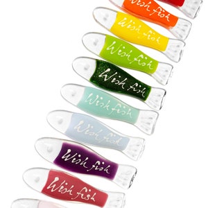 May include: A set of ten glass fish ornaments in various colors, each with the words "Wish Fish" written on them in white. The fish are arranged in a rainbow pattern, starting with red and ending with pink.