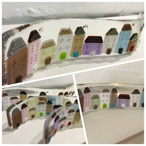 May include: A glass art piece featuring a row of colourful houses with white and black details. The houses are arranged in a curved line on a clear glass base.