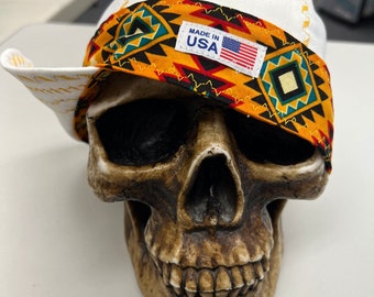 May include: White bandana with a colorful geometric pattern and the text "Made in USA" on a yellow label. The bandana is on a skull.