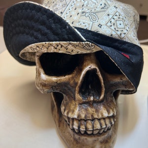 Op de afbeelding: Een witte schedel met een zwart-witte bandana-hoed. De hoed heeft een paisley-patroon.