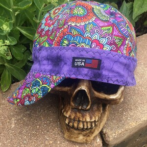 Puede incluir: Una gorra de soldadura de color morado y con estampado paisley multicolor, con una visera morada y una etiqueta "Made in USA".