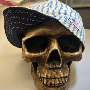 May include: A blue and white striped baseball cap with a navy blue brim and a "Made in USA" label. The cap is sitting on top of a skull.