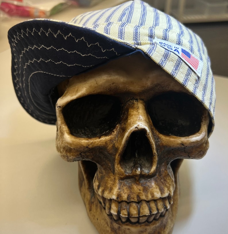 May include: A blue and white striped baseball cap with a navy blue brim and a "Made in USA" label. The cap is sitting on top of a skull.