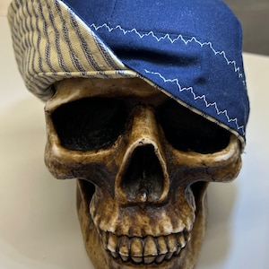 May include: A blue and white striped baseball cap with a blue brim. The cap is sitting on a skull.