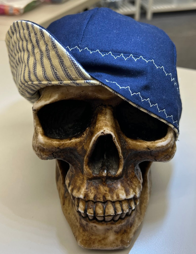 May include: A blue and white striped baseball cap with a blue brim. The cap is sitting on a skull.