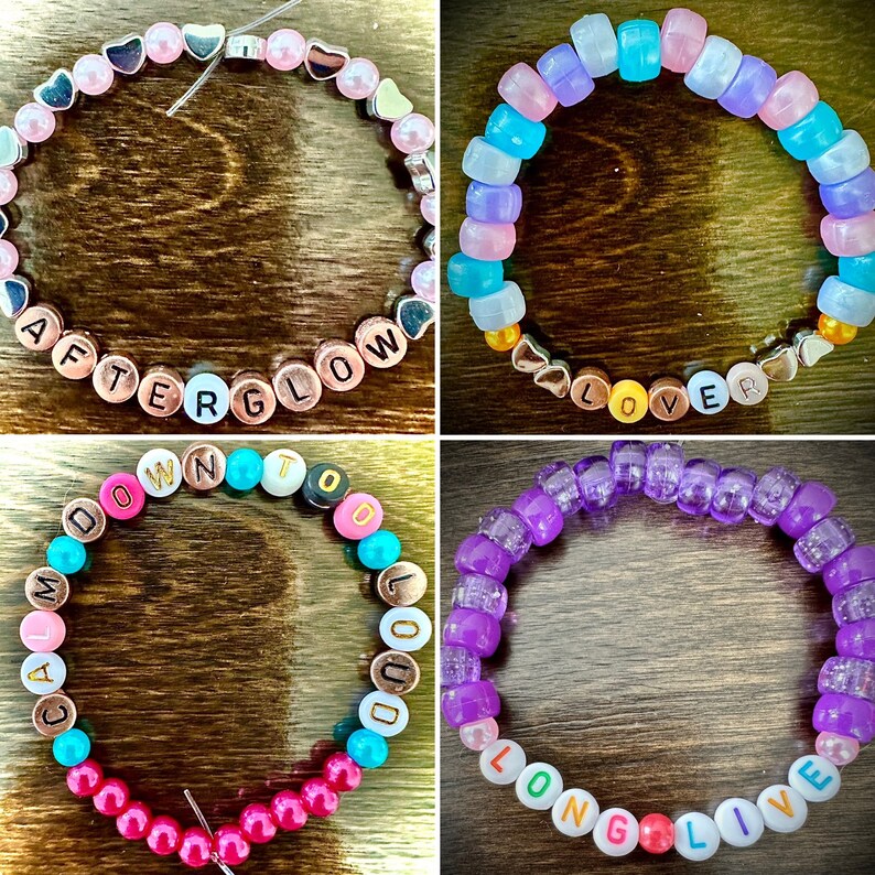May include: Four colorful beaded bracelets with different words spelled out on them. The bracelets are pink, purple, blue, and multi-colored. The words on the bracelets are "Afterglow", "Lover", "Long Live", and "Calm Down To Loud".