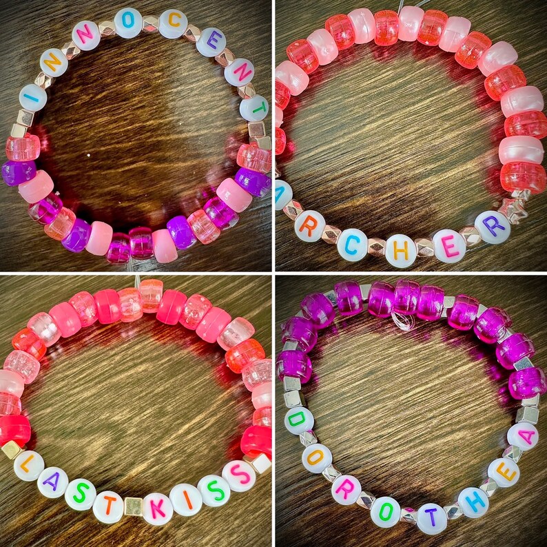 May include: Four colorful beaded bracelets with different words spelled out on them. The bracelets are made with pink, purple, and white beads. The words on the bracelets are "INNOCENT", "ARCHER", "LAST KISS", and "DOOR THEA".