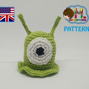 May include: Green crocheted amigurumi toy with a large white eye and a black pupil. The toy is shaped like a slug with two long antennae. The toy is on a white background. The text "PATTERN" is visible in the image.